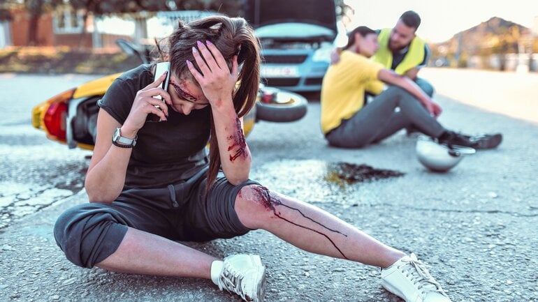 Eine junge Frau hatte einen Unfall, sie hält sich den Kopf und ruft den Rettungsdienst