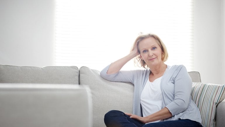 Eine Frau mittleren Alters sitzt auf einem Sofa.