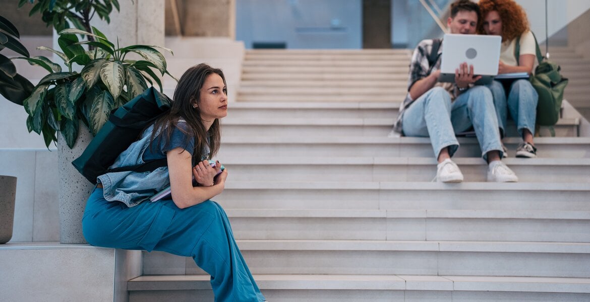 Junge Frau sitzt abseits von anderen Menschen auf einer Treppe und wirkt sozial distanziert – Symbolbild für schizoide Persönlichkeitsstörung