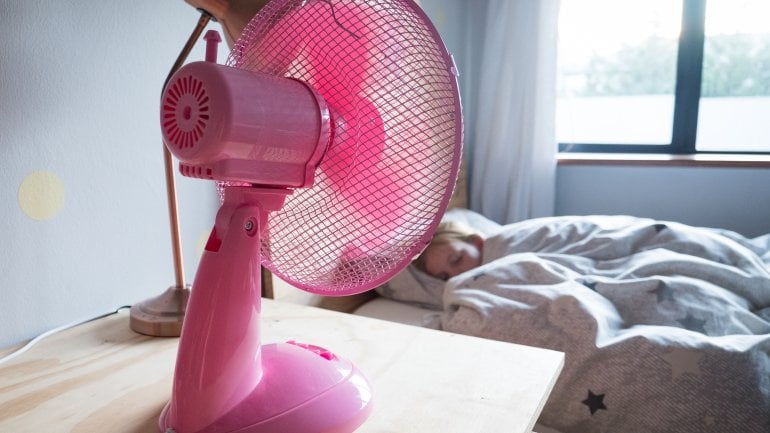 Ein Mädchen schläft im Bett, daneben ein Ventilator.