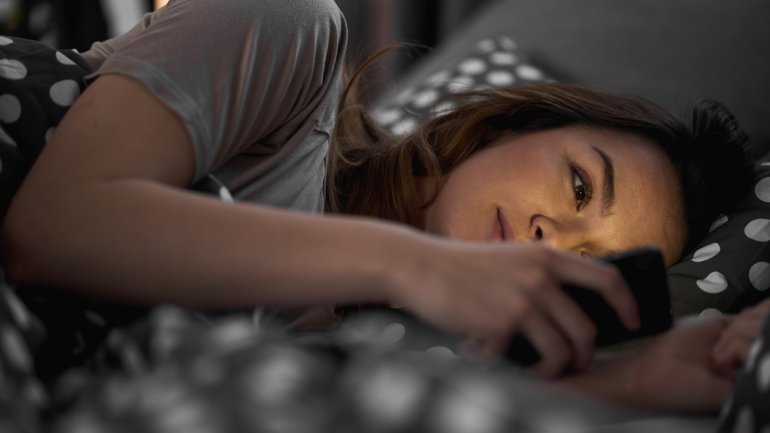 Eine junge Frau liegt im Bett und schaut auf ihr Smartphone.