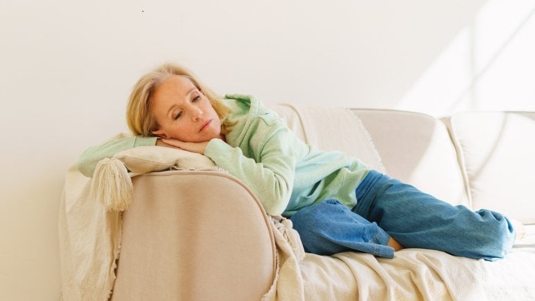 Frau liegt müde auf Sofa und leidet unter Schlafstörungen während der Wechseljahre.