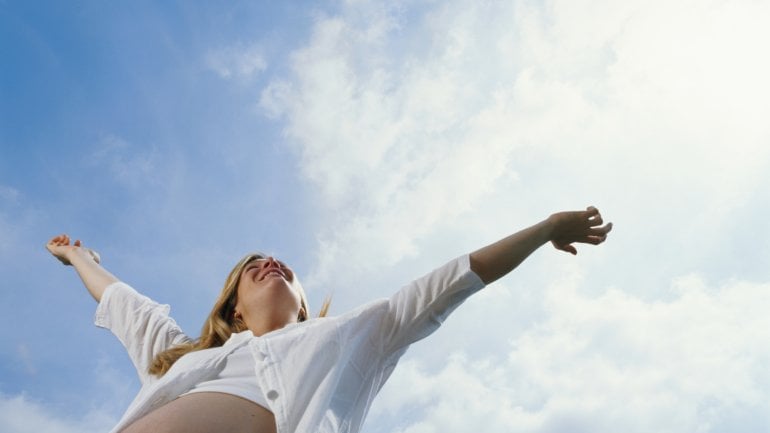 Eine Schwangere streckt die Arme zum Himmel.