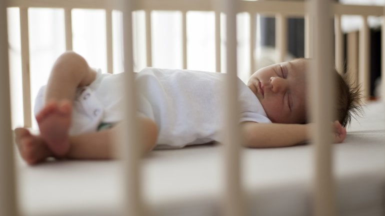 Ein Baby liegt schlafend in einem Gitterbett.