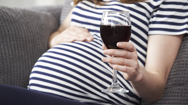 Eine schwangere Frau hält ein Glas Rotwein in der Hand.