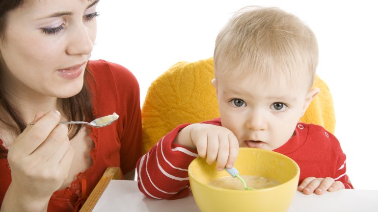 Das Bild zeigt eine Frau, die ein Kleinkind füttert.