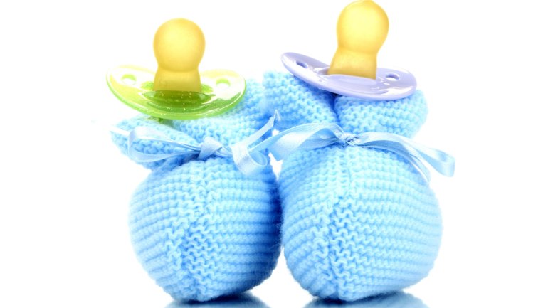 Das Bild zeigt ein Paar blaue Babyschuhe und zwei Schnuller.