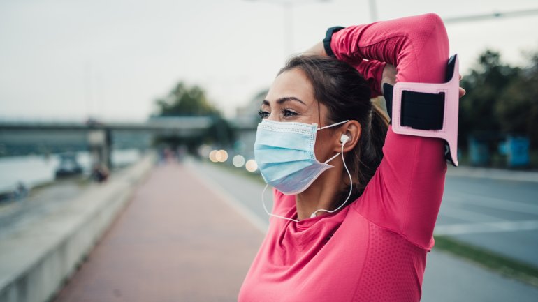 Eine Frau mit Mund-Nasen-Maske dehnt sich nach dem Laufen.