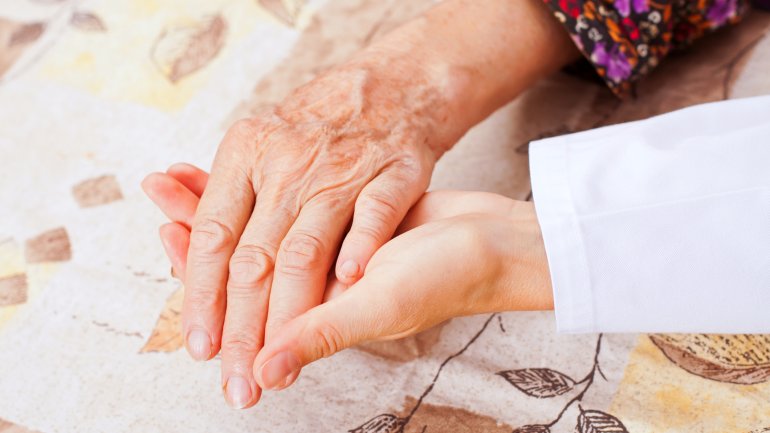 Die Hand eines Senioren hält die Hand einer jüngeren Person.
