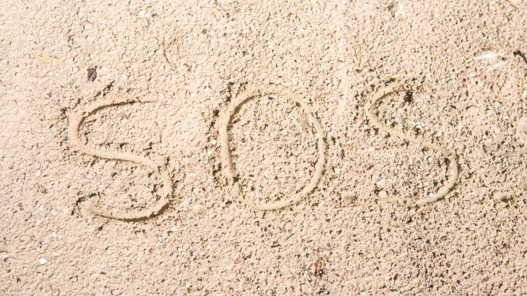 Im Sand ist das Wort SOS geschrieben.