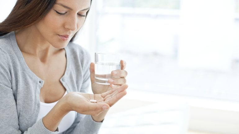 Tabletten einnehmen: Frau hält ein Glas Wasser und eine Tablette in der Hand