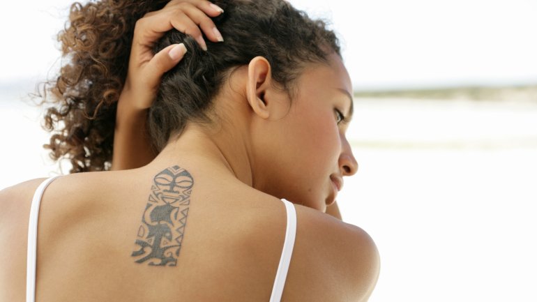 Dunkelhaarige Frau mit einem Tattoo zwischen den Schulterblättern.