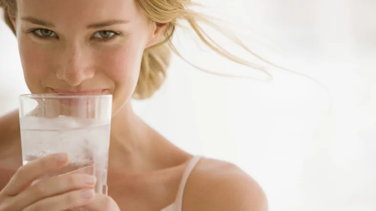 Das Bild zeigt eine Frau, die ein Glas mit Wasser und Eiswürfeln hält.