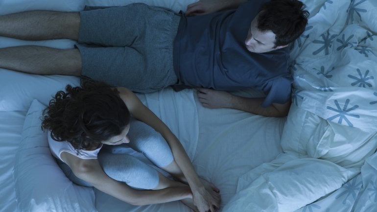 Ein Mann und eine Frau sitzen im Bett und streiten.