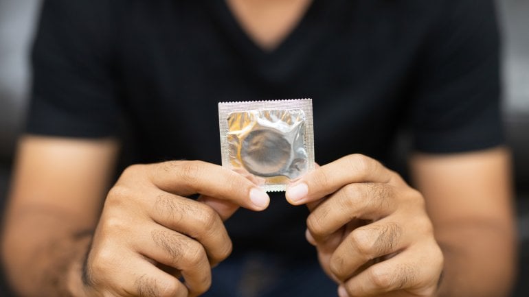 Mann hält Kondom in den Händen, um sich vor Tripper zu schützen.