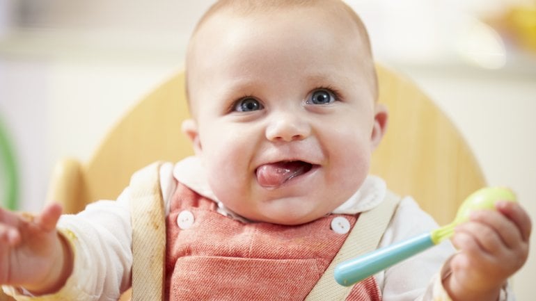 Ein fröhliches Baby hält einen Löffel.