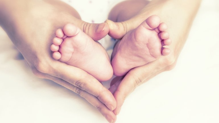 Eine Frau umschließt mit ihren Hände kleine Babyfüße.
