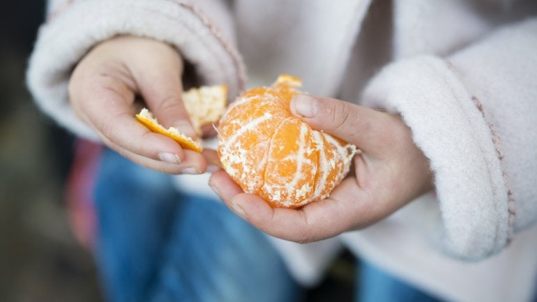 Ein Mädchen schält eine Mandarine