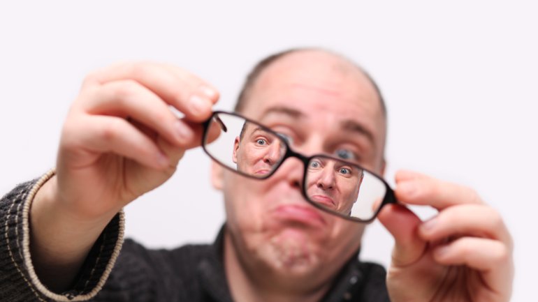 Das Bild zeigt einen Mann durch eine Brille betrachtet.