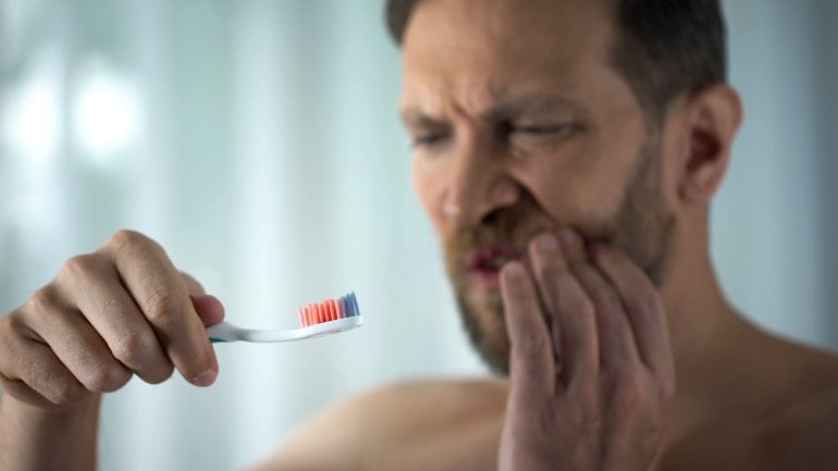 Mann putzt sich die Zähne und hat Blut auf der Zahnbürste
