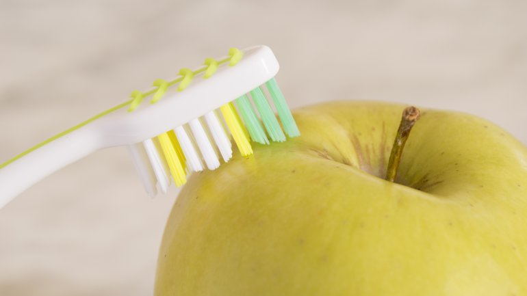 Das Bild zeigt eine Zahnbürste und einen Apfel.