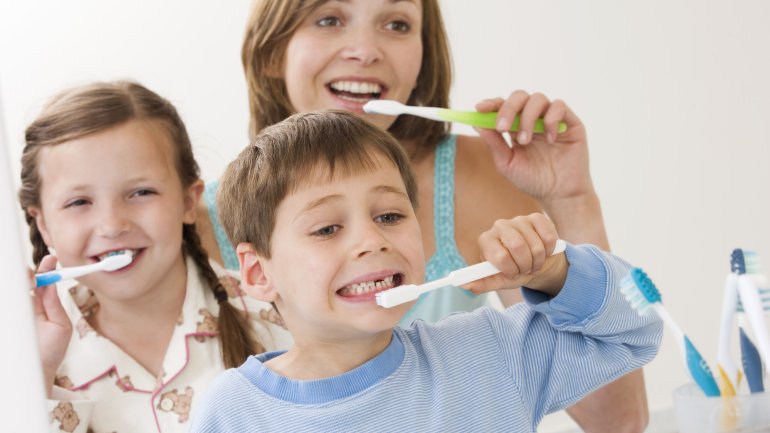 Das Bild zeigt eine Frau, einen Jungen und ein Mädchen beim Zähneputzen.