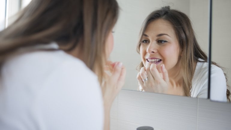 Frau guckt sich im Spiegel Zahnverfärbung an.
