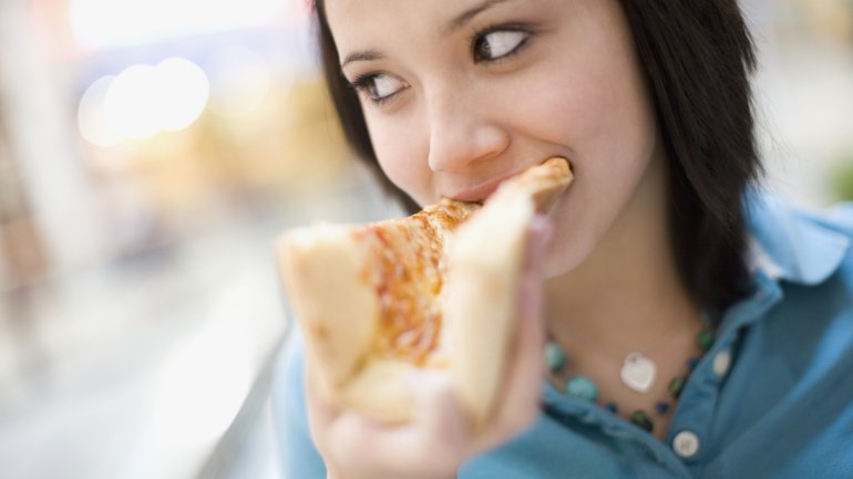 Eine Frau beißt in ein Stück Pizza.