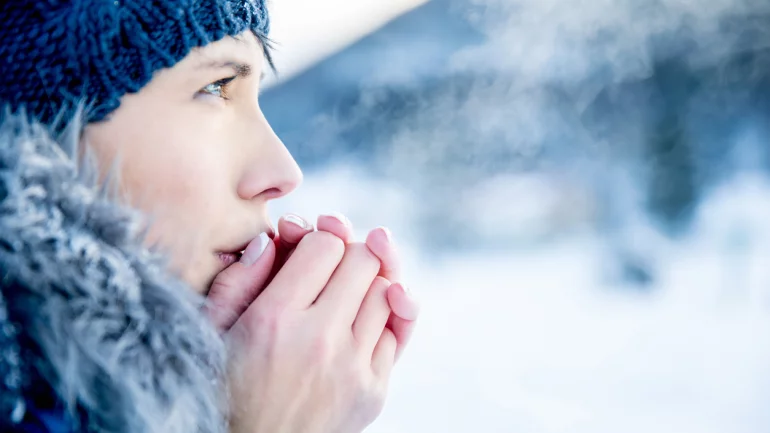 Eine winterlich gekleidete Frau wärmt ihre Hände durch Anhauchen.