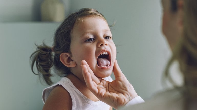 Ein kleines Mädchen streckt für eine Halsuntersuchung die Zunge raus